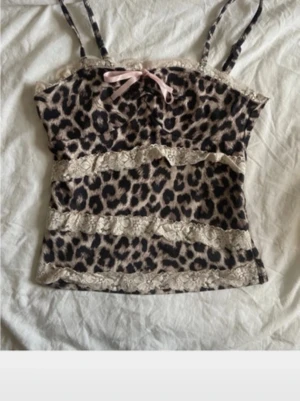 Leopardmönstrad spetslinnetopp - Säljer en leopardmönstrad linnetopp med tunna axelband, dekorerad med beige spetsdetaljer och en söt rosa rosett framtill. Toppen har en croppad passform och är perfekt för dig som gillar trendiga statement-plagg.