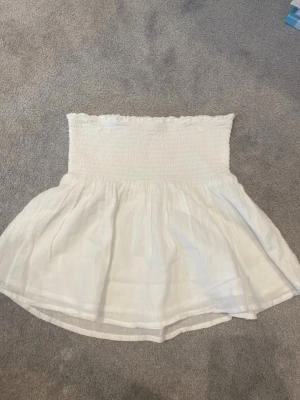 Vit bandeau tubtopp i bomull - Säljer en söt vit bandeau tubtopp i luftig bomull. Toppen har smockad överdel och ett flowy fall nedtill, perfekt för varma dagar. Stilren och enkel att matcha med jeans eller kjol.