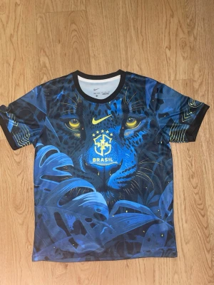 Nike Brasil blå matchtröja pantermotiv - Säljer en riktigt snygg matchtröja från Nike med Brasil-logga och ett stort blått pantermotiv på framsidan. Tröjan har rund hals, korta ärmar och är gjord i ett lätt, andningsbart material. Färgerna är blå, svart och gul med coola detaljer och tryck.
