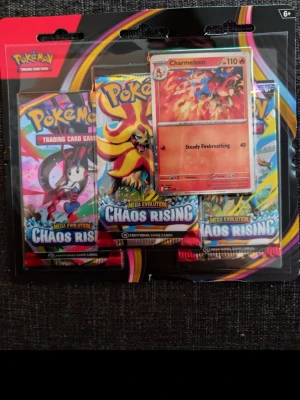 Pokémon Chaos Rising boosterpaket - Säljer ett Pokémon Mega Evolution Chaos Rising boosterpaket med tre booster packs och ett Charmeleon promo-kort. Förpackningen har färgglad design med motiv av olika Pokémon och är perfekt för samlare eller TCG-spelare.