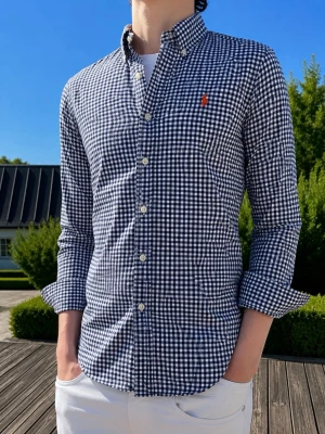 Rutig skjorta från Ralph Lauren - (MODDELEN ÄR 185 och väger 75kg)Klassisk rutig skjorta från Ralph Lauren i mörkblått och vitt. Skjortan har lång ärm, knappar framtill och den ikoniska broderade loggan på bröstet. Tillverkad i bomull för en skön och luftig känsla. Perfekt till jeans eller chinos.