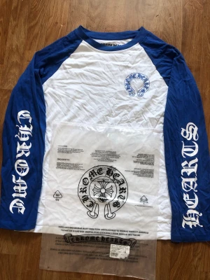 Blå långärmad  t-shirt - Säljer en blå och vit långärmad t-shirt med tryck på ärmarna och bröstet samt stort CH-tryck på ryggen. Klassisk baseballmodell med kontrastfärgade ärmar och coola loggor. Perfekt för dig som gillar streetwear och vill sticka ut. Pris kan diskuteras 