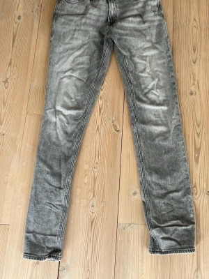 Gråa raka jeans från jack&jones - Säljer ett par gråa jeans från jack&jones med klassisk rak passform och fem fickor. Jeansen har en snygg tvättad look och detaljer som synliga sömmar och läderpatch bak i midjan. Perfekta för en avslappnad och trendig stil. Storlek 30/34, modell: regular/clark