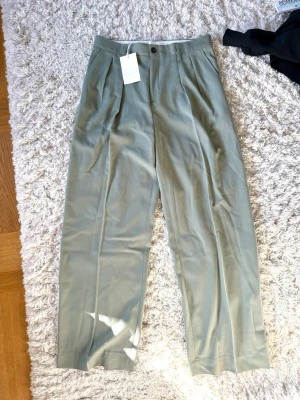Ljusgröna kostymbyxor - Snygga ljusgröna kostymbyxor från fillipa k med hög midja och pressveck. Byxorna har vida ben och klassisk knappgylf. Perfekta för en clean och stilren look. Materialet är mjukt och har en lätt glans.