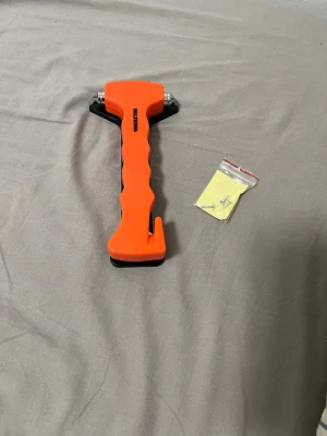 Nödhammare orange med bälteskniv - Säljer en orange nödhammare från WELMA med inbyggd bälteskniv och metallspetsar för att krossa bilrutor. Handtaget är ergonomiskt utformat i plast och verktyget kommer med monteringsfäste och skruvar. Perfekt att ha i bilen för extra säkerhet.