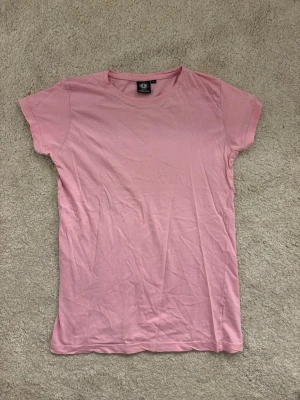 Ljusrosa t-shirt från Tribute - En enkel och stilren ljusrosa t-shirt från Tribute. Klassisk rund halsringning och korta ärmar. Tillverkad i mjuk bomull som känns skön mot huden. Perfekt basplagg att matcha med jeans eller kjol.