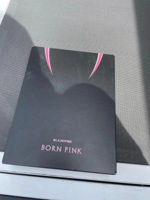 BLACKPINK Born Pink albumbok - Säljer en exklusiv albumbok från BLACKPINK med titeln Born Pink. Omslaget är svart med rosa detaljer och innehåller en rosa CD-skiva. Perfekt för fans av K-pop och samlare av musikrelaterade böcker och merchandise.