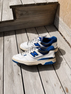 New Balance 550 vita/blå sneakers - Säljer ett par New Balance 550 sneakers i vitt och blått. Skorna är använda relativt lite, och inga deffekter finns. Strorlek: 42
