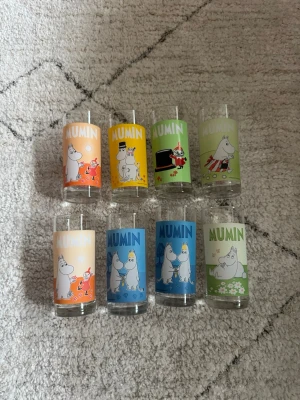 Mumin glas 8-pack med färgglada motiv - Säljer ett set med åtta glas med olika färgglada Mumin-motiv. Glasen har tryck i orange, gul, grön, blå och beige med olika karaktärer från Muminvärlden. Perfekta för dig som gillar samlarprylar eller vill ha något unikt till köket.
