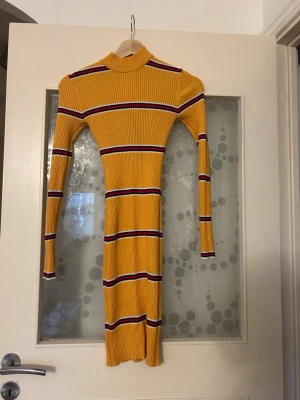Gul ribbad klänning från BikBok - Säljer en ribbad, kroppsnära gul klänning från BikBok i storlek XS. Klänningen har lång ärm, hög hals och horisontella ränder i vitt, marinblått och rött. Perfekt för dig som gillar färg och vill sticka ut lite extra.