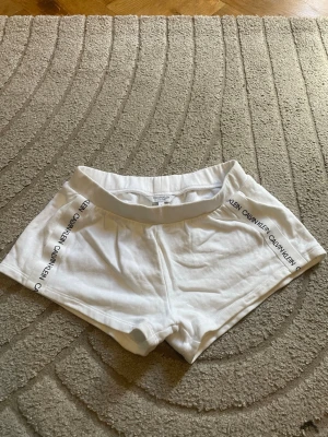 Vita shorts från Calvin Klein - Snygga vita shorts från Calvin Klein med logga längs sidorna. De har en elastisk midja och är tillverkade i mjukt bomullsmaterial för en bekväm känsla. Perfekta för en avslappnad och sportig stil.