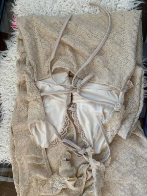 Beige spetsklänning med volanger - Supersöt beige klänning i spets med volangdetaljer och knytband i ryggen. Klänningen har en v-ringad urringning, smala axelband och är figurnära. Perfekt för sommarens alla tillfällen!  Storlek S&M