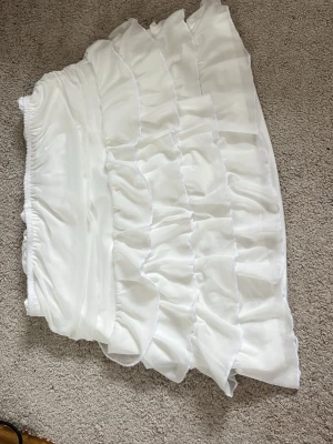 Vit volangkjol med resårmidja - Säljer en superfin vit kortkjol med flera lager volanger och elastisk midja. Den här inbyggda shorts så dom är säkra om man säger så! Kjolen har en luftig och flowy känsla, perfekt för varma dagar. Materialet känns lätt och bekvämt mot huden. Enkel att matcha med olika toppar för en trendig look. Köpte den för 300 säljer den för 189 och använt endast 1 gång så är i bra skick🤞🏽❤️ den är i storlek S men kommer också funka för xs för att den är tajt 