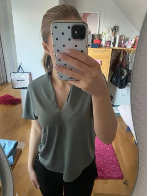 Grågrön blus med v-ringning - Säljer denna superfina grågrön blus med v-ringning och korta ärmar. Från H&M, storlek S!!💞💞💞