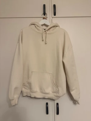Bik Bok - Säljer en beige oversized hoodie med stor känguruficka framtill och dragsko i huvan. Hoodien har ribbade muddar vid ärmslut och nederkant. Perfekt för dig som gillar en enkel och clean stil. Materialet känns mjukt och skönt mot huden.