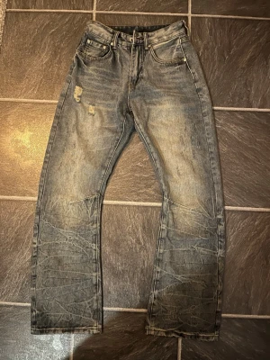 Bootcut jeans - Säljer ett par blåa bootcutjeans med rak passform och slitningar på låret. Jeansen har en klassisk femficksmodell och tydliga tvättade detaljer för en cool, avslappnad look. Materialet är denim i bomull och de har en vintagekänsla. Dem är helt nya men är lite små i storleken. Skick 10/10
