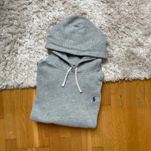 Grå hoodie från Polo Ralph Lauren - Snygg grå hoodie från Polo Ralph Lauren med klassisk huva och dragsnören i storlek D. Tröjan har en liten mörkblå logga broderad på bröstet. Hoodien är i mycket bra skick!😃 hör gärna av er vid frågor