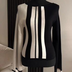 Finstickad tröja med mönster - Säljer en unik stickad tröja i svart och vitt randigt mönster framtill och baktill. Tröjan har lång ärm och en asymmetrisk design som verkligen sticker ut. Toppen har även vida ärmar. Supersnyggt plagg som passar till alla tillfällen