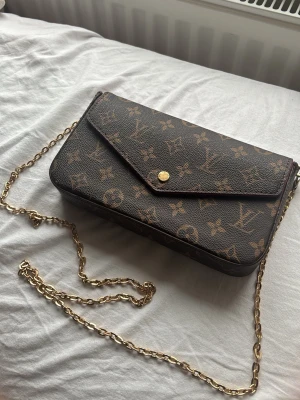 Snygg märkes väska  - Säljer en  märkes väska med guldfärgad kedjerem. Väskan har kuvertformad flärp med tryckknapp och är tillverkad i tåligt canvasmaterial. Perfekt för dig som vill ha en lyxig och tidlös accessoar. Pris kan diskuteras !🤎👜💸