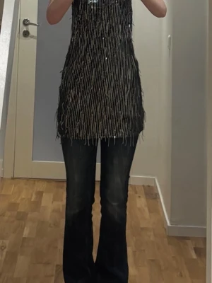 Svart glittrig paljettklänning - Säljer en svart halterneckklänning med glittriga paljetter. Snyggt fall och coolt mönster av paljetter som reflekterar ljuset. Den är från pull and bear i storlek M och använd en gång.