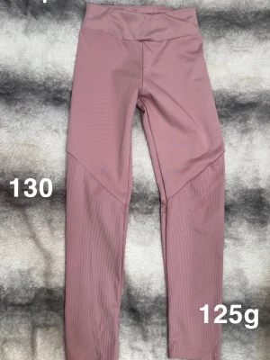 Rosa ribbade leggings med hög midja - Säljer ett par snygga rosa leggings med hög midja och ribbade detaljer på benen. De är tillverkade i ett stretchigt material som sitter bekvämt och följsamt. Perfekta för dig som vill ha både stil och komfort.🌸 Sparsamt använda. Storlek 130