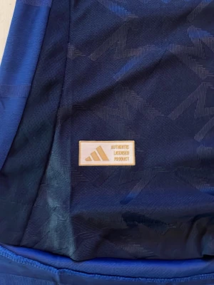 Manchester United blå matchtröja Adidas - Snygg blå Manchester United matchtröja från Adidas med Snapdragon-logga på bröstet. Tröjan har autentisk licensmärkning, diskret mönster i tyget och klubbmärke på vänster sida. Perfekt för fotbollsträning eller att bära som supporter.