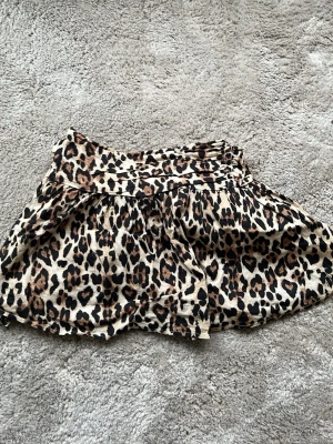 Kort leopardmönstrad kjol - Säljer en kort kjol med leopardmönster i beige, brunt och svart. Kjolen har bred resår i midjan och ett lätt, fladdrigt tyg som ger en snygg siluett. Är i barn stolek ! Använd väldigt få gånger ca 2 gånger kanske!