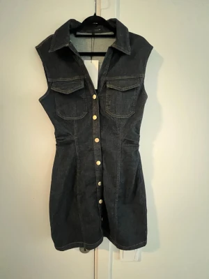 Ärmlös jeansklänning med knappar - Snygg mörkblå ärmlös jeansklänning från Zara med krage och tryckknappar framtill. Samt en dragkedja i sömmen på ena sidan som inte syns. Ny och aldrig använd med prislapp kvar