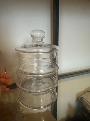 Staplingsbar glasburk med lock - Säljer en genomskinlig staplingsbar glasburk med tre separata fack och ett matchande lock. Perfekt för förvaring av småsaker, snacks eller smycken. Enkel och stilren design som passar i de flesta rum.