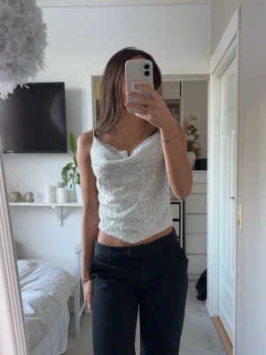 Glittrig silver topp med smala axelband - Säljer en glittrig silverfärgad topp med smala axelband och draperad urringning. Toppen är i bra skick storlek XS/S