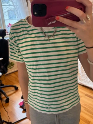 Randig grön och vit t-shirt - Säljer en fräsch t-shirt med gröna och vita ränder. T-shirten har korta ärmar, rund halsringning och en avslappnad passform. Perfekt för en chill vardagslook och enkel att matcha med jeans eller shorts.