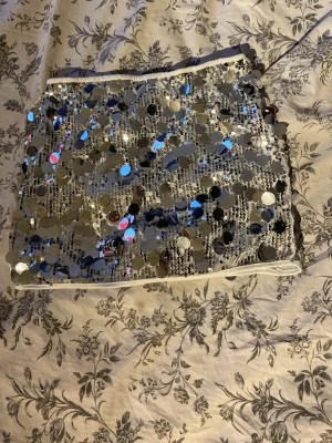 Glittrig silverkort kjol med paljetter - Supersnygg kort kjol i silver med massor av stora och små paljetter som ger en riktigt glittrig effekt. Perfekt för dig som vill sticka ut och glänsa! Kjolen har en rak passform och är fodrad för extra komfort.