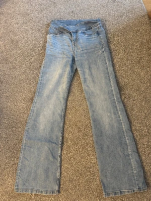 Ljusblå bootcut jeans från H&M med dubbla knappar - Snygga ljusblå bootcut jeans med dubbla knappar i midjan och dragkedja från H&M. Jeansen har klassisk femficksdesign och är tillverkade i mjukt denimtyg. Perfekta för en avslappnad och trendig look.