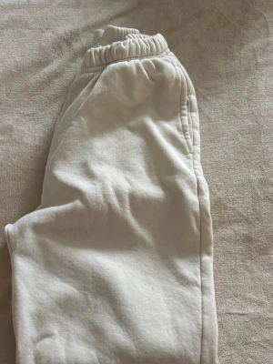 Ljusa mjukisbyxor Gina Tricot - Ett par gräddvita/ljusbeiga mjukisbyxor med resår i midjan och raka ben. Perfekta för en avslappnad stil, och super sköna!😚Är i storlek Xs men passar S också.