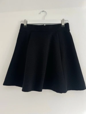 Svart kjol  - Fin svart kjol i ett lite randigt tyg (se bild). Använd endast ett fåtal gånger så i väldigt fint skick! Bak på kjolen finns där en silvrig dragkedja 🥰