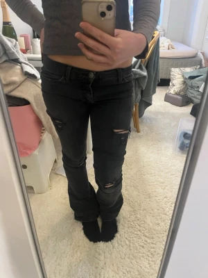 Svarta slitna jeans med hål - Säljer ett par svarta jeans med slitningar och hål på låren och knäna.Perfekta för en avslappnad och trendig look.