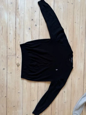 Svart stickad tröja Polo Ralph Lauren - Klassisk svart stickad tröja från Polo Ralph Lauren med rund halsringning och broderad logga på bröstet. Tröjan är i 100% bomull och har en stilren, tidlös design med långa ärmar och ribbade muddar. Inga synliga tecken på användning! Ny pris c:a 2500kr