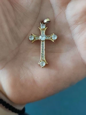 Guldigt korshalsband med stenar stål - Ett snyggt halsband med ett korsformat hänge i guldfärg, dekorerat med gnistrande vita stenar på varje spets och i mitten. Perfekt för dig som gillar klassiska och stilrena smycken med lite extra bling.