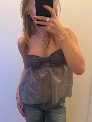 Grå axelbandslös topp med rosett - Snygg grå axelbandslös topp med söt rosettdetalj framtill. Den är sydd av mig!! Ställ gärna prisförslag och kika gärna på mina andra annonser!!🩷💕