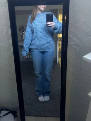 Blå stickad tröja med ballongärmar - Säljer en ljusblå stickad tröja med ballongärmar och rund hals. Tröjan är grovstickad och har en avslappnad passform, perfekt för att hålla sig varm. Materialet ser ut att vara mjukt och bekvämt, troligen akryl eller ullblandning.