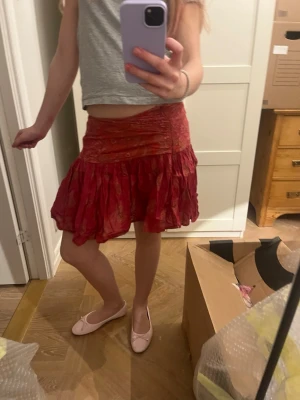 Röd volangkjol med omlott - Säljer en röd/rosa kjol med volanger. Kjolen har ett lätt, flowy tyg och ett subtilt mönster i olika röda nyanser. Storlek S/XS, mycket bra skick! 