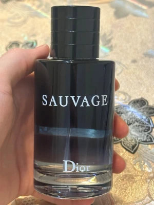 Dior Sauvage Eau de Toilette 100ml - Säljer en Dior Sauvage parfym med elegant svart och genomskinlig glasflaska. Flaskan har en stilren, rund form och silverfärgad sprayfunktion med Dior-logga på toppen. En ikonisk doft för dig som gillar exklusiva parfymer. 100ml magnet lock