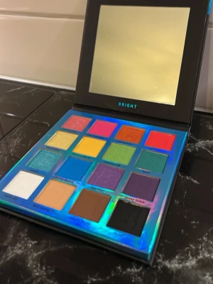 Beauty bay Bright ögonskuggspalett med spegel - Färgstark ögonskuggspalett från Beauty bay med 15 intensiva nyanser i både matta och skimrande finish. Paletten innehåller allt från neonrosa, orange och blått till gult, grönt och klassiskt svart och vitt. Praktisk spegel i locket och holografisk förpackning.