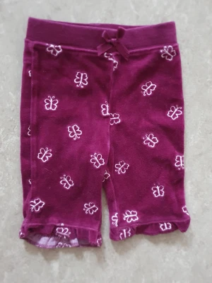 Shorts - Söta lila shorts med vita fjärilar och en liten rosett i midjan. Shortsen har elastisk midja och volangkant nertill. Perfekta för varma dagar och ger en lekfull vibe.