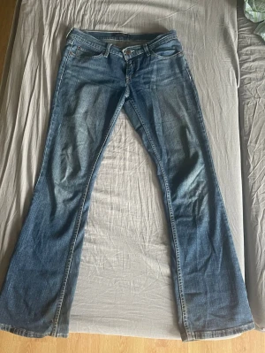 Blå bootcut jeans från Levi's - Säljer ett par blå super lågmidjade bootcut jeans från Levi's med 4 fungerande fickor. Jeansen har en ikonisk läderpatch bak i midjan och kontrastsömmar. Perfekta för dig som gillar retrostil. De har lite slitning längst ner men det är inget man tänker på. Säljer pga av att de är för små för mig. Jeansen har ingen storleks lapp men skulle säga att de är i storlek 34-36 men det  beror på hur tajt man vill ha det vid låren.
