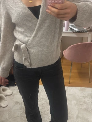 & Other stories omlottkofta - Mysig beige stickad omlottkofta med knytband i midjan. Koftan har långa ärmar, ribbade muddar och en mjuk, fluffig känsla. Perfekt att slänga över en topp för en avslappnad men snygg look.