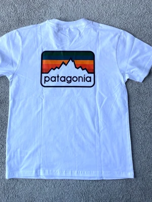 Patagonia vit t-shirt, storlek M - T-shirt från Patagonia med kort ärm och rund halsringning. Tröjan är vit med en liten Patagonia-logotyp på vänster bröst och en större logotyp på ryggen.  T-shirten är i mycket fint skick.   Herrmodell