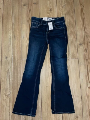 Mörkblå bootcut jeans från 157 - Snygga mörkblå bootcut jeans från 157 med klassiska fyra fickor och kontrastsömmar. Jeansen har utsvängda ben och låg midja, perfekta för en trendig och avslappnad look. Materialet är stretchigt denim som ger skön passform.