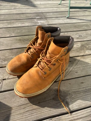 Timberland kängor storlek 39 - Säljer ett par klassiska bruna Timberland kängor i läder med robust sula och bruna snören. Kängorna har vadderad mörkbrun kant upptill och tydlig Timberland-logga på sidan. Perfekta för höst och vinter.