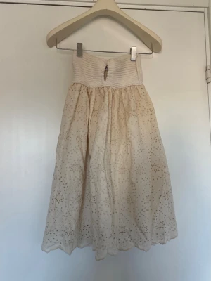 Beige klänning med broderade detaljer - Söt beige badeuklänning med ribbad topp och broderade blommor i kjolen. 